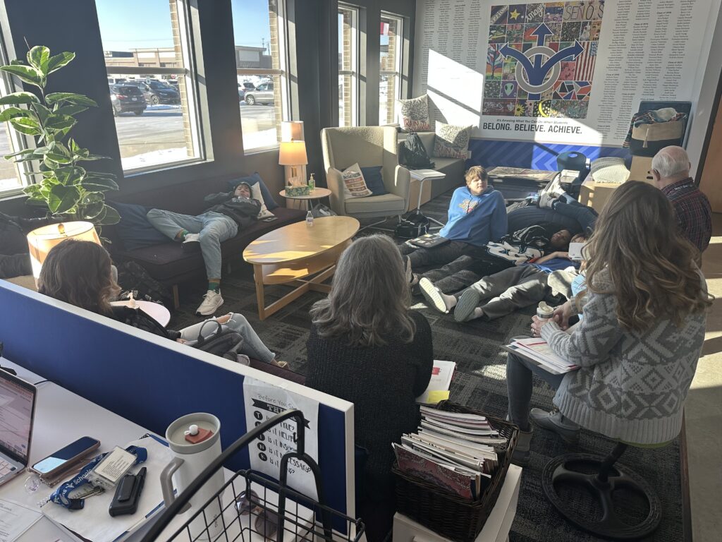 Students sit on couches and the floor listening to a speaker